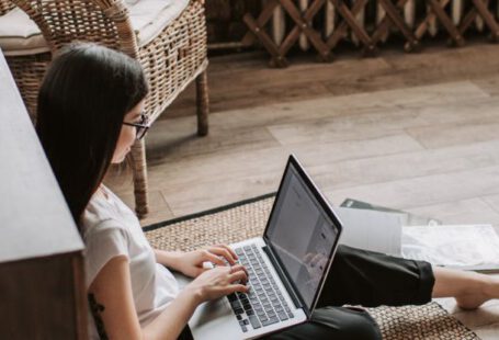 Referral Programs - Young barefoot woman using laptop on floor near books in stylish living room