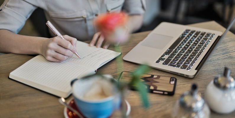 Content Marketing - Person Writing On A Notebook Beside Macbook